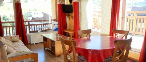 A cozy room with a wooden dining table, four chairs, a sofa, and a TV on a stand.