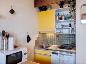 Kompakti keittiö, jossa on mikroaaltouuni, pesuallas ja liesi. Astiat on sijoitettu telineeseen, ja seinällä on ripustettava kattilapidikkeen.