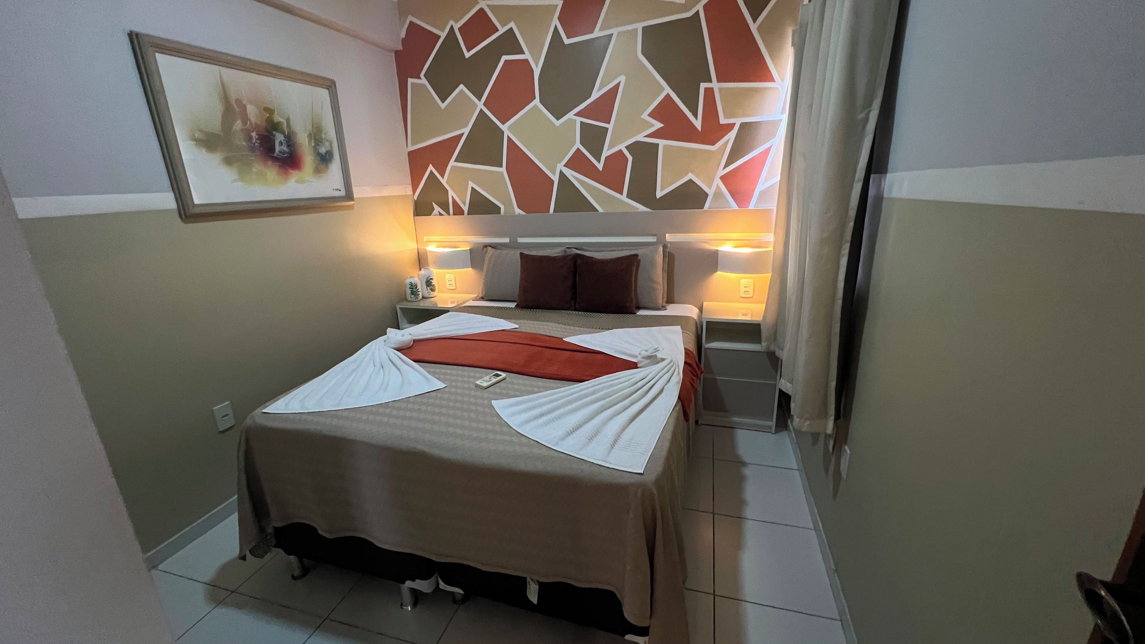 A hotel room with a bed, bedside tables, a wall-mounted painting, and a geometric-patterned wall.