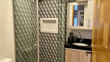 Un baño con cabina de ducha de vidrio, inodoro, lavamanos con encimera negra y armarios de madera.