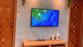 Ein Zimmer mit einem an einer Marmorwand montierten Fernseher, einem Holztisch mit zwei roten Hocker und einer Kommode mit Schubladen.
