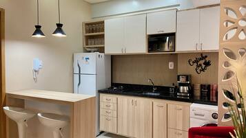 Una cocina moderna con microondas integrado, refrigerador y cafetera. Hay una encimera de madera con un lavamanos y una silla roja.