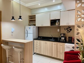 Eine moderne Küche mit eingebauter Mikrowelle, einem Kühlschrank und einer Kaffeemaschine. Es gibt eine Holzausziehtafel mit einem Spülbecken und einem roten Stuhl.