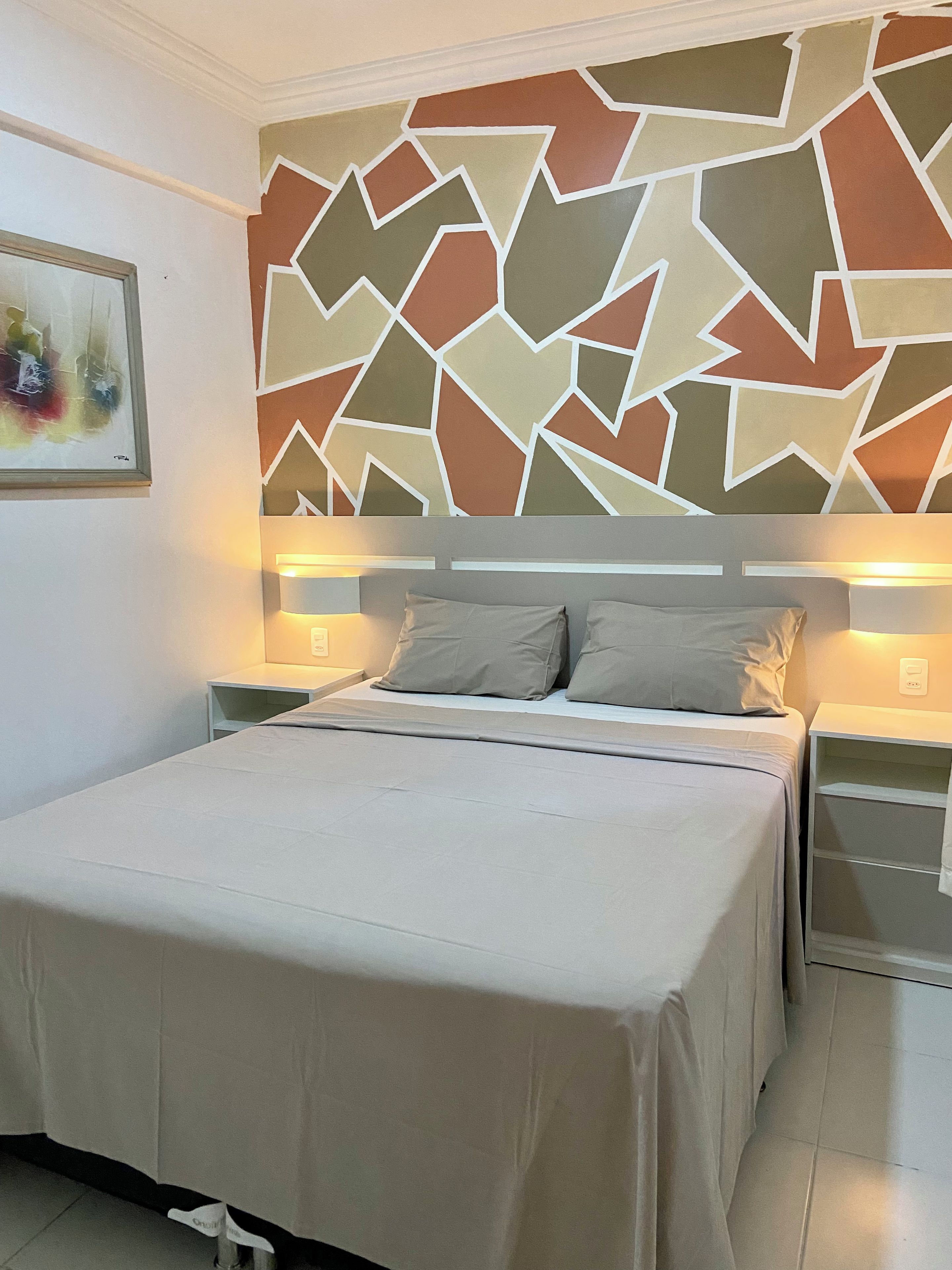 A bedroom with a bed, two bedside tables, a wall with a geometric pattern, and a painting on the wall.