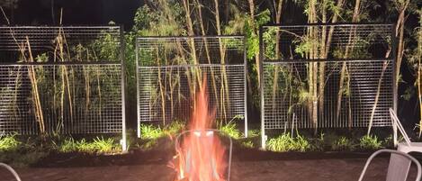 An outdoor seating area with a fire feature, surrounded by a metal fence and trees.
