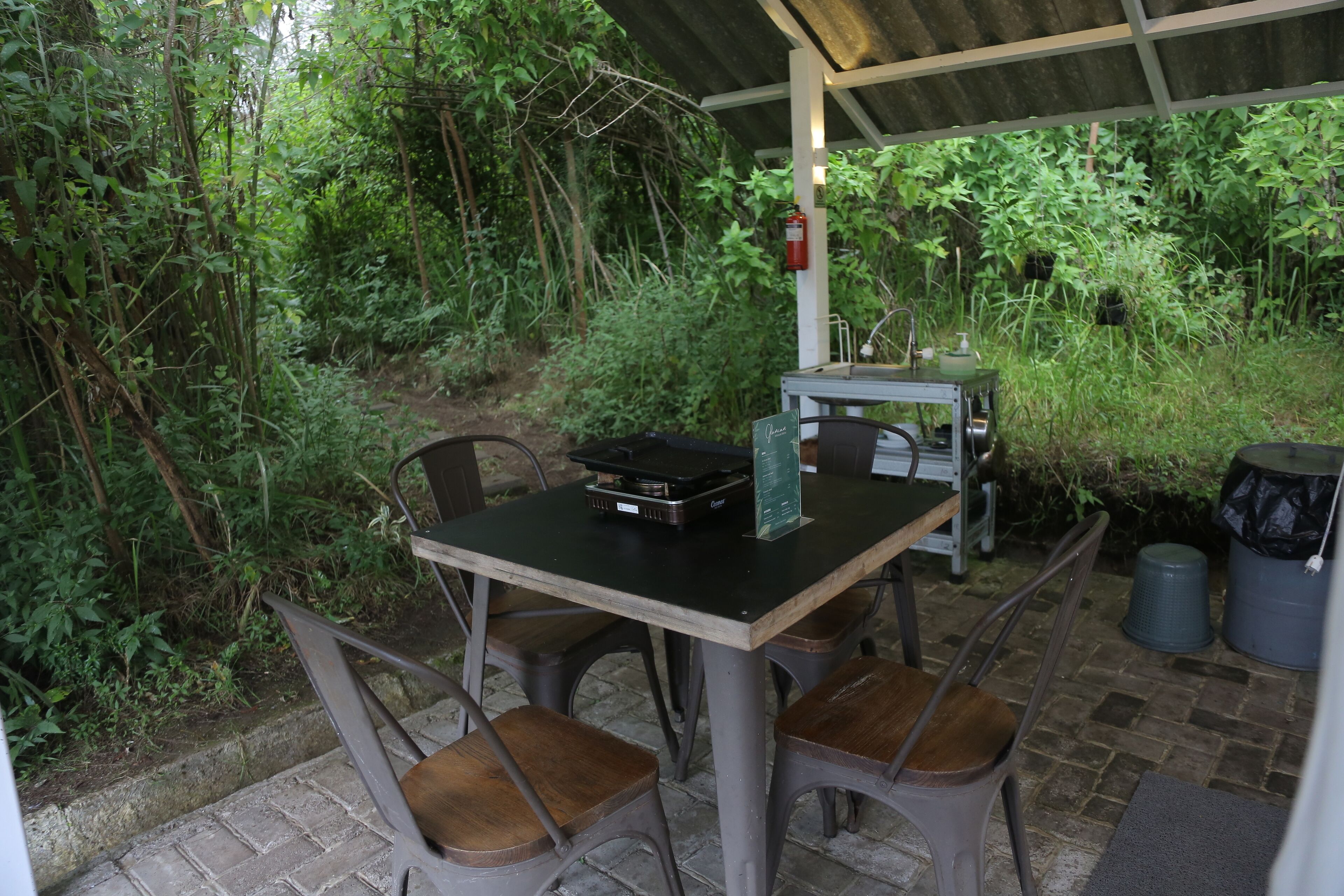 Un patio al aire libre con una mesa y sillas, rodeado de abundante vegetación.
