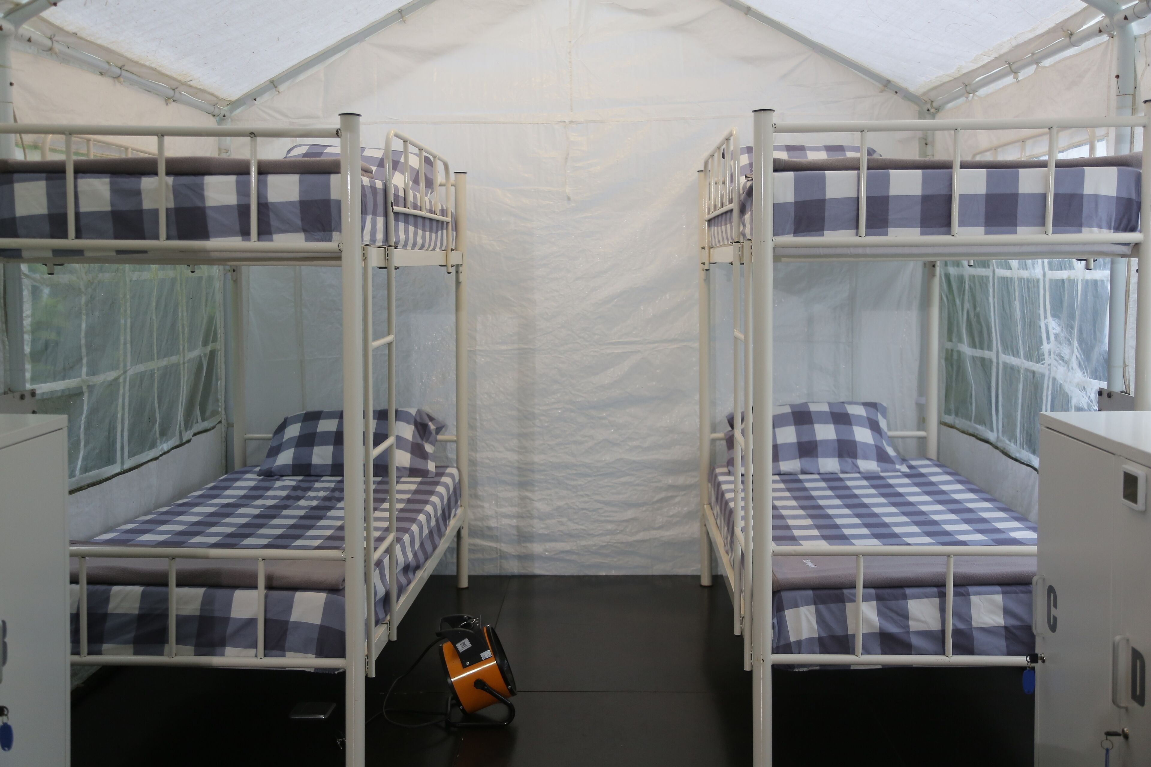 Alojamento em tenda com duas beliches, cada uma com roupa de cama xadrez e almofadas.