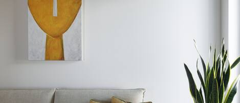 Uma sala de estar moderna com um sofá cinza, duas almofadas amarelo-mostarda, uma grande pintura abstrata e uma planta em vaso.