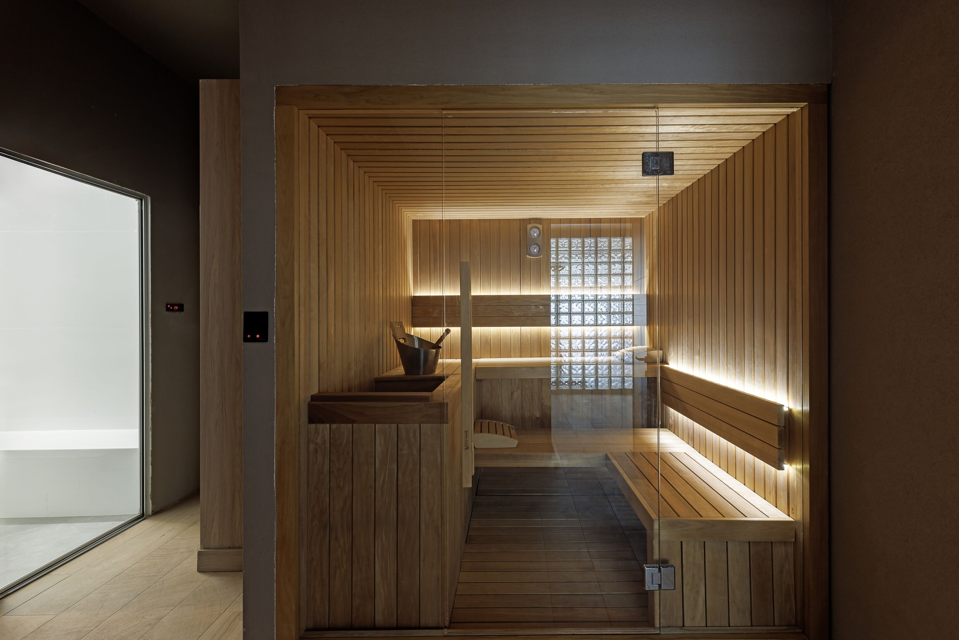 A sauna with wooden walls and benches, a small table with a bowl, and a window with a grid pattern.
