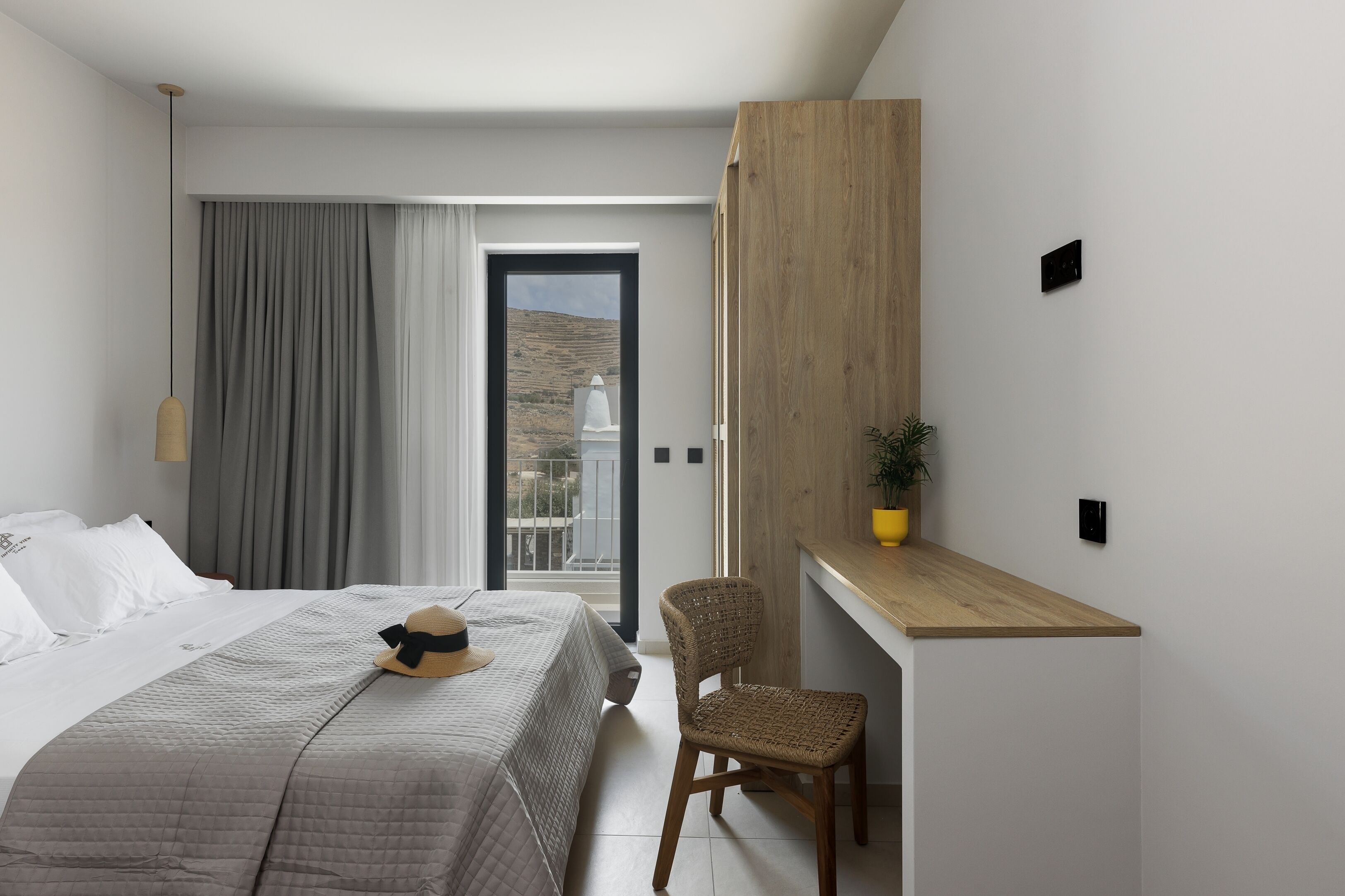A modern hotel room with a bed, a desk, a chair, and a view of a hill.