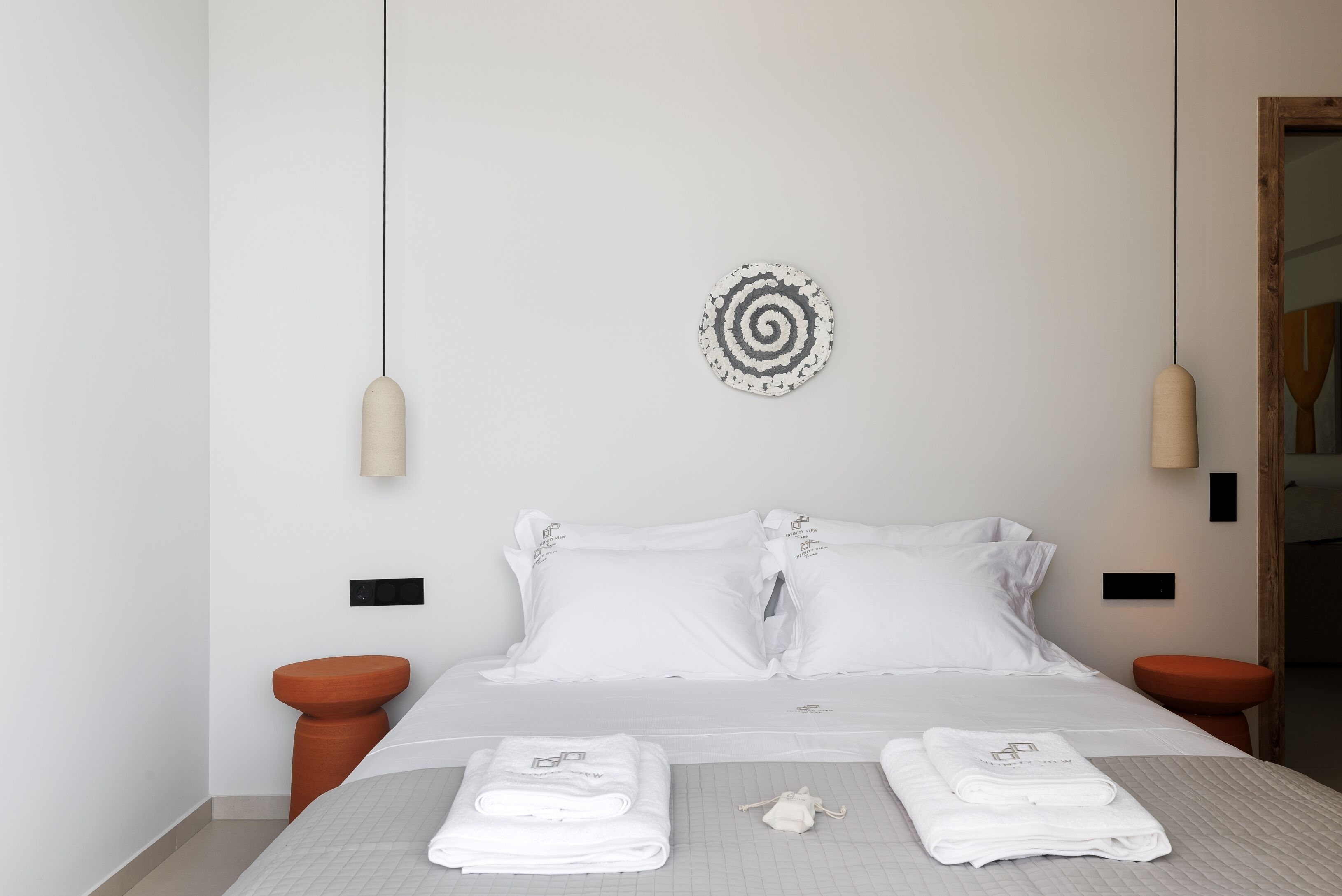 A neatly made bed with white linens and pillows, a round wall decoration, and two bedside tables with lamps.