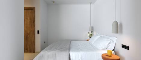 Un dormitorio minimalista con cama, mesita de noche y lámpara colgante.