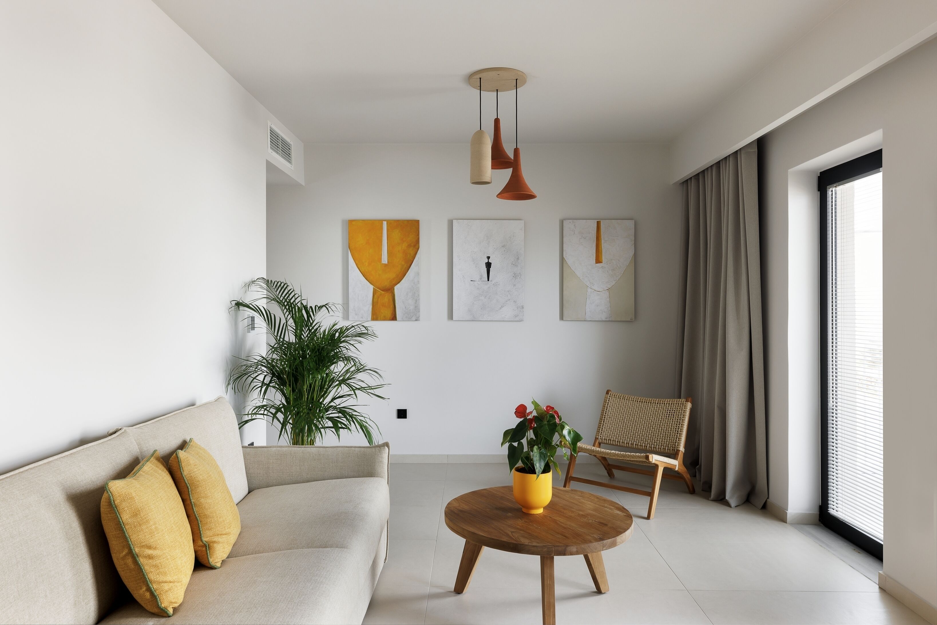 A modern living room with a sofa, a round wooden coffee table, a potted plant, and abstract wall art.