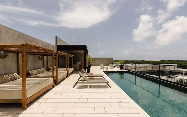 Un espace piscine aménagé sur le toit, avec des chaises longues, une pergola en bois et une vue sur le panorama urbain.