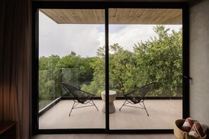 Un balcon avec deux chaises au design épuré, dont l’armature est en fil de fer noir, et une table ronde, offrant une vue sur un paysage verdoyant et luxuriant.
