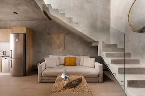 A modern living room with a sofa, a decorative rug, a wall hanging, and a staircase.