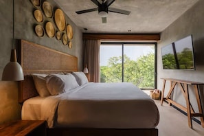 Une chambre à coucher moderne, dotée d’un grand lit, d’un ventilateur de plafond, d’une télévision et offrant une vue sur les arbres par la fenêtre.