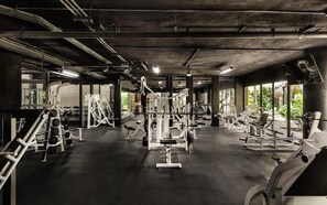 Ein Fitnessraum mit verschiedenen TrainingsgerĂ€ten, groĂen Fenstern und einer Betondecke.