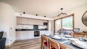 A modern kitchen with white cabinets, a dining table set for four, and a view of the outdoors through large windows. - 100m from resort center, 2nd floor, view mountain/village, balcony, tv, 69m², Morzine (Morzine)