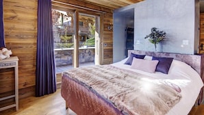 Une chambre avec un grand lit, des murs en bois, une vue à travers des portes vitrées et une petite table sur laquelle est posé un vase.