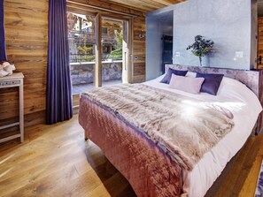 Ein Schlafzimmer mit einem großen Bett, Holzwänden, Blick durch Glastüren und einem kleinen Tisch mit einer Vase.