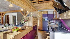 Une cuisine moderne avec des poutres en bois, un îlot central agrémenté d’un panier de fruits et un four encastré.