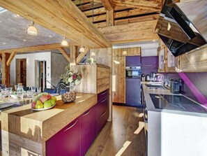 Eine moderne Küche mit Holzbalken, einer zentralen Kochinsel mit Obstschale und einem eingebauten Backofen.