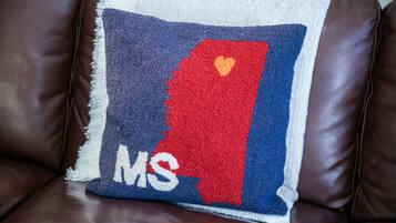 A brown leather sofa with a square cushion featuring a red and blue design with the letters "MS" and a heart symbol.