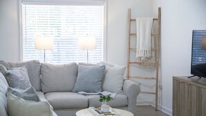 A living room with a grey sofa, a round coffee table with a tray and a plant, a wooden ladder, and a television on a wooden cabinet. - The Pappy, 2BR House by Velvet Ditch Villas (Oxford)