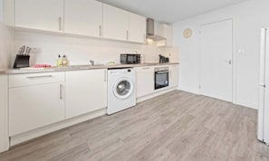 Een moderne keuken met witte kasten, een wasmachine, een magnetron en een oven.