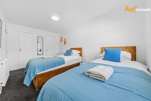 Habitación de hotel con dos camas, cada una con cubrecama azul y cabecero de madera. Se observa un armario blanco y un espejo en la pared.