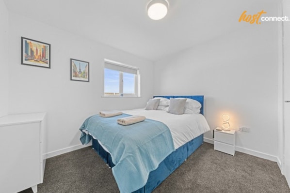 Een slaapkamer met een bed, een nachtkastje, een raam en twee ingelijste foto’s aan de muur.