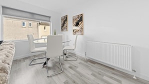 Een moderne kamer met een eettafel, stoelen, een bank en een radiator.