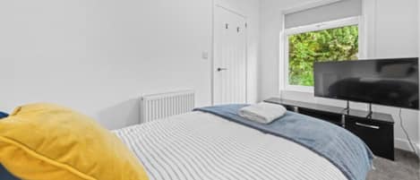 A bedroom with a bed, a television, a window, and a radiator.