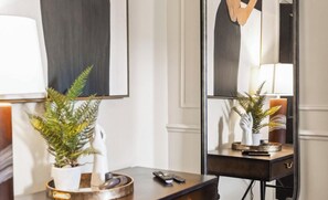 Ein Zimmer mit Schreibtisch, Topfpflanze, Fernbedienung und Spiegel, der eine Lampe und eine Statue widerspiegelt.