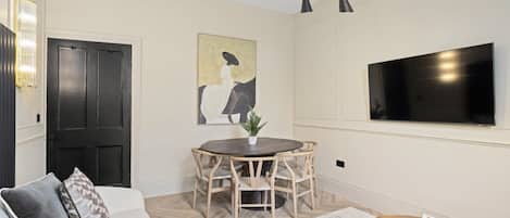 Una sala de estar moderna con una mesa de comedor redonda, un sofá, un televisor y una araña.