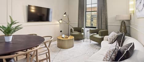 A modern living room with a round dining table, two sofas, a coffee table, and a TV mounted on the wall.