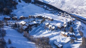 Un village de montagne enneigé, avec ses bâtiments traditionnels en bois, ses pistes de ski et une vue dégagée sur les montagnes environnantes.