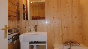 Pieni kylpyhuone, jonka seinät ovat puuta, ja jossa on valkoinen pesuallas, peili ja kylpyamme.