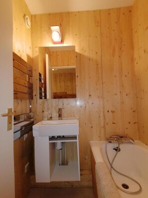 Ein kleines Badezimmer mit Holzwänden, einem weißen Waschbecken, einem Spiegel und einer Badewanne.