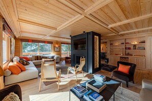 A cozy log cabin interior with a fireplace, wooden furniture, and a bookshelf.