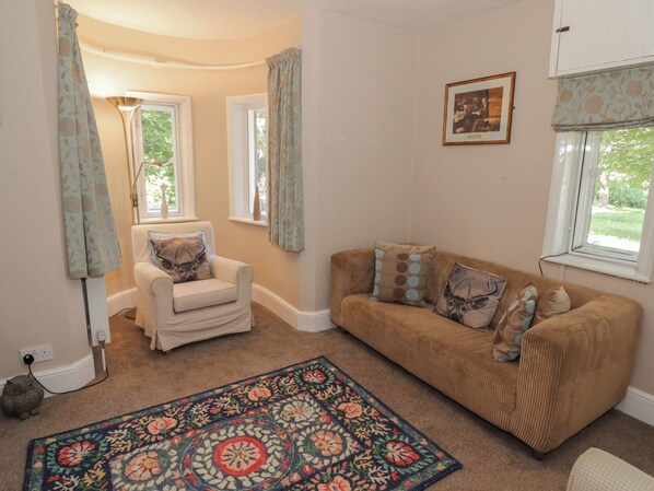 A cozy living room with a beige sofa, a patterned armchair, and a floral area rug. - Boxbush Lodge (Monmouth)