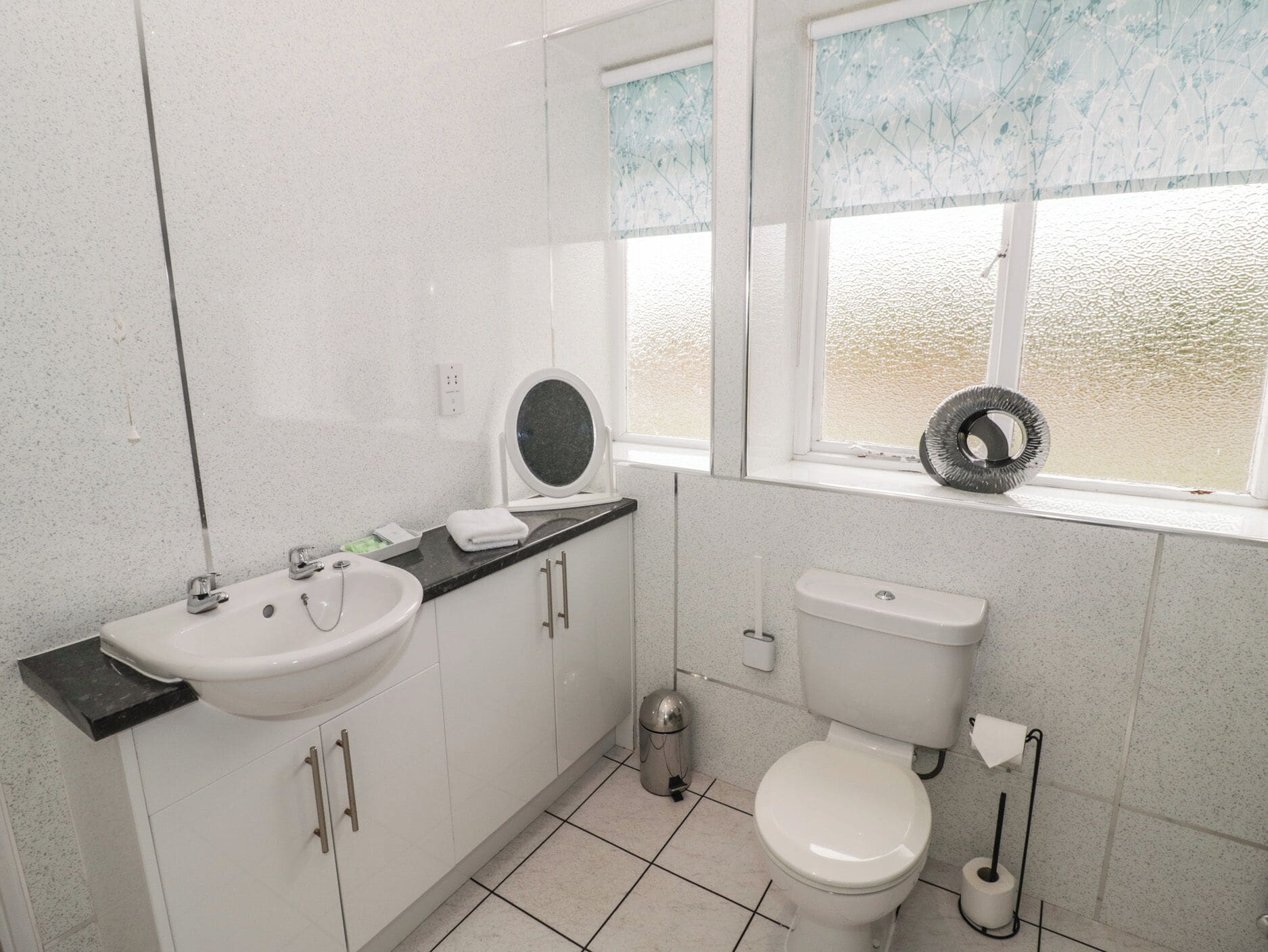 Un baño con lavamanos, espejo, inodoro y ventana con vistas.