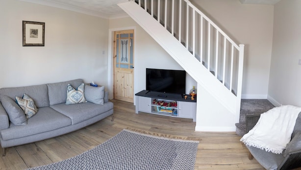 A living room with a grey sofa, a television on a stand, a staircase, and a door with a window. - Deer Hill Grove (York)