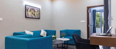 A modern living room with two blue sofas, a small round table, a black chair, and a laptop on a wooden desk.