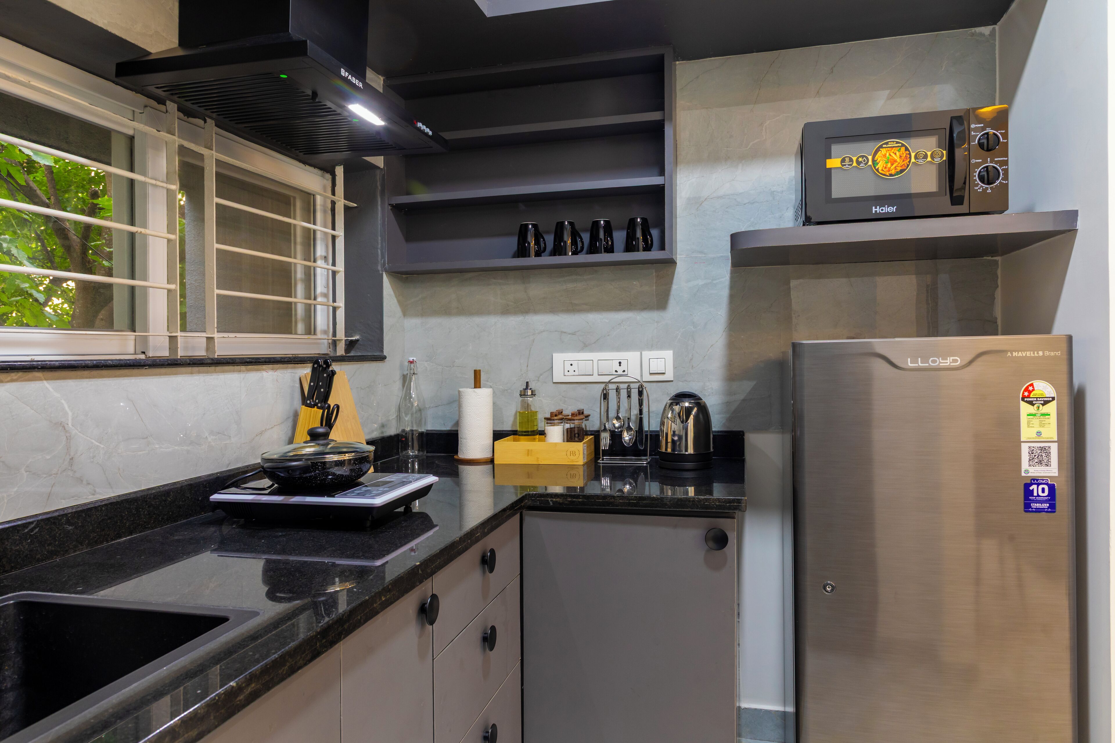A modern kitchen with a stainless steel refrigerator, a microwave, and a window with blinds.