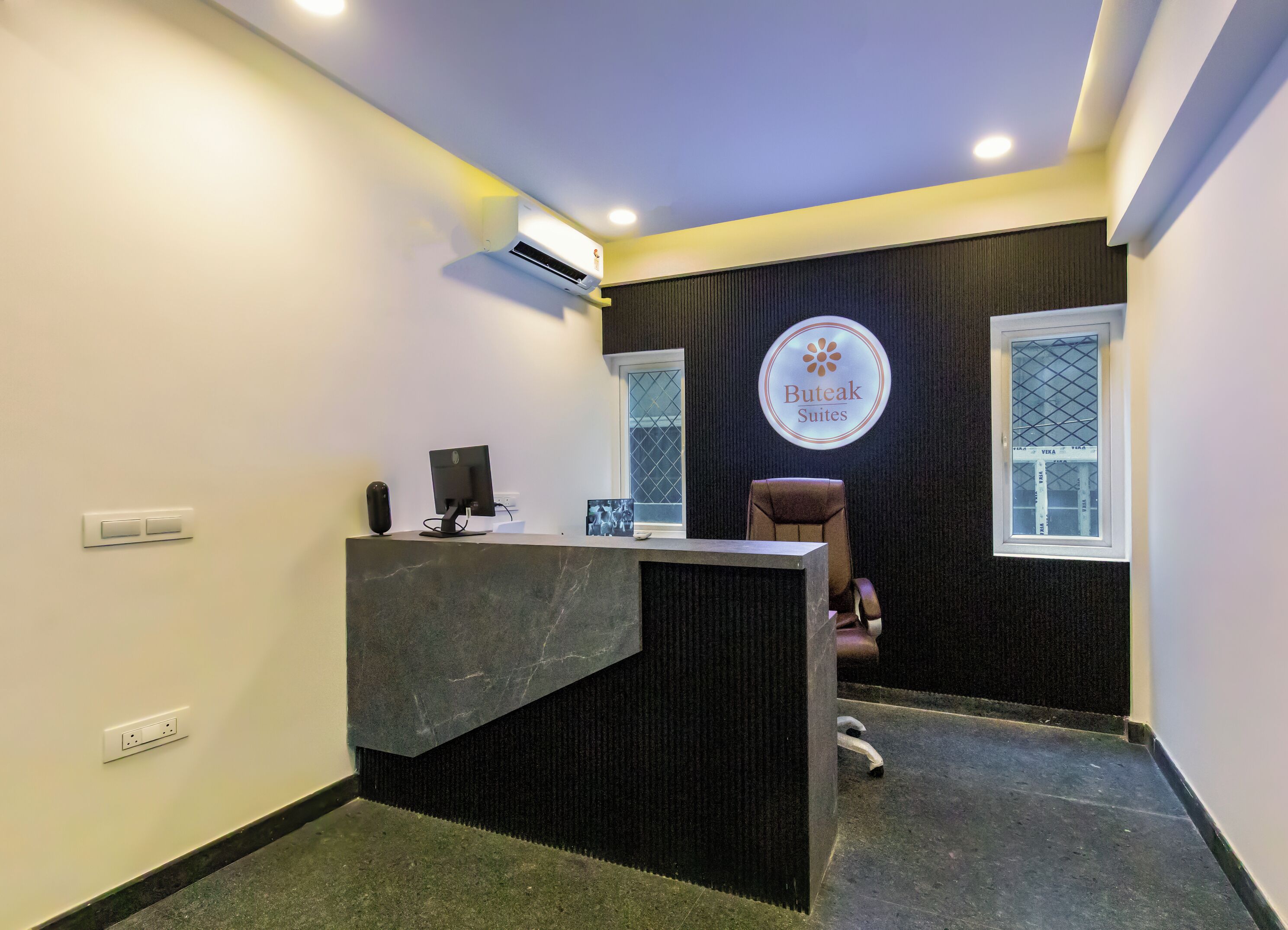A reception area with a desk, computer, and a chair. There is a sign on the wall and a window with a view.