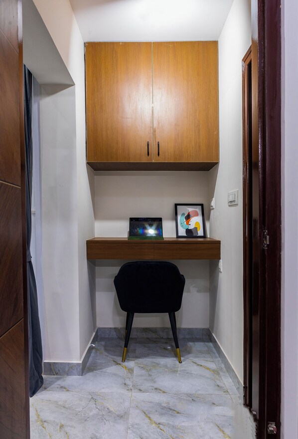 A corner room with a wooden cabinet, a desk with a chair, and a framed picture. - Buteak Suites (Bengaluru)