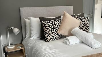 A neatly made bed with a grey headboard, a bedside table with a lamp, and three framed artworks on the wall.