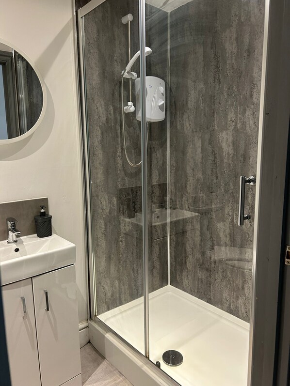 Une salle de bain moderne avec une douche à parois de verre, un lavabo blanc doté d’un distributeur de savon et un miroir au-dessus du lavabo.